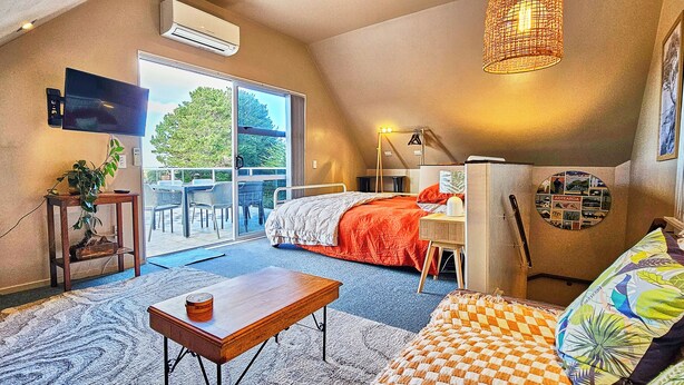 Ein gemütliches Zimmer mit Bett, Schreibtisch, Sessel, Fernseher und einem großen Fenster.