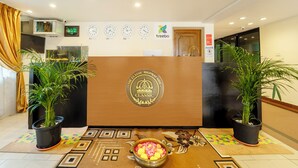 A reception area with a wooden reception desk, potted plants, a clock, and a digital display. -  Treebo Classic Highway Side (Thiruvananthapuram)