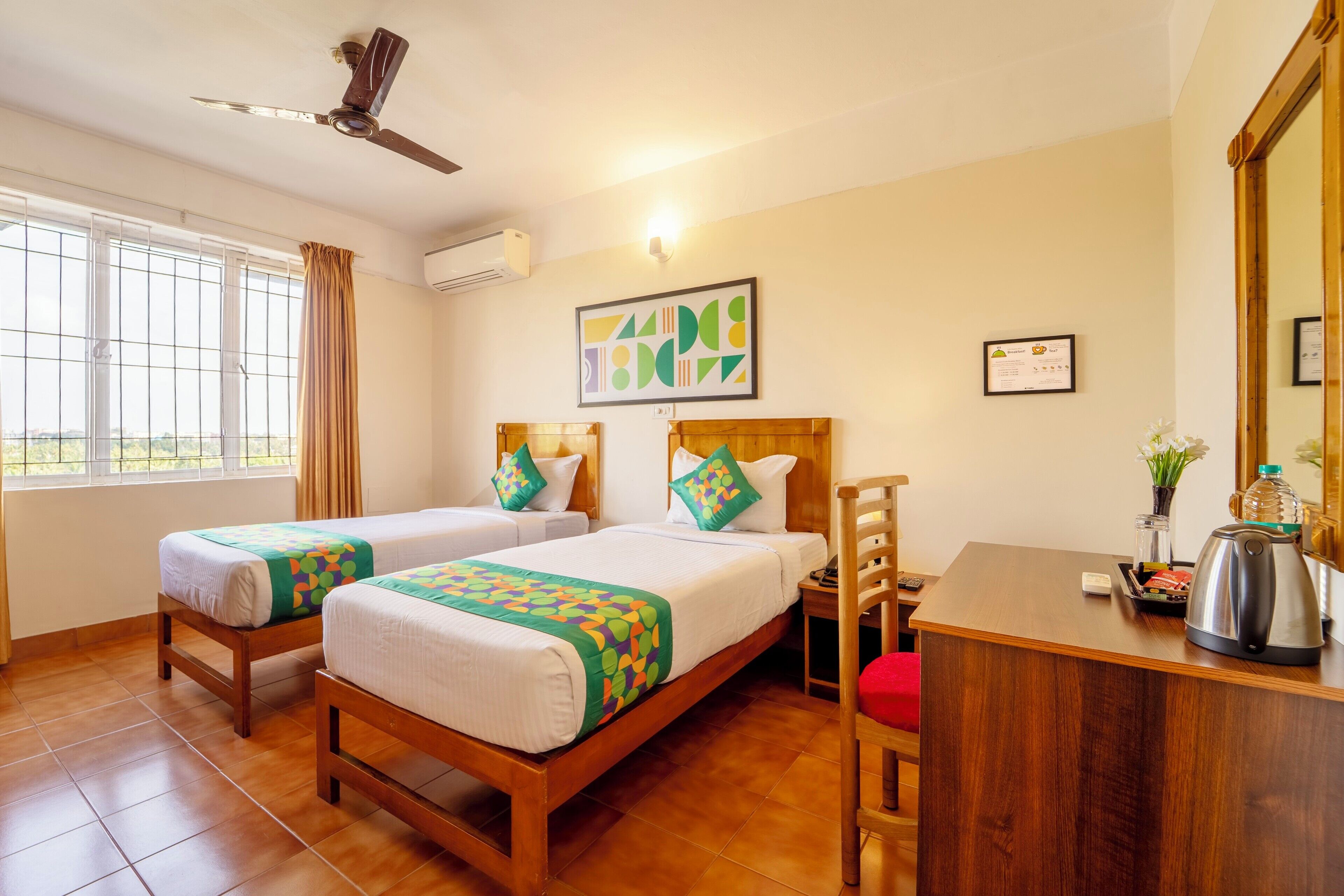 A hotel room with two beds, a desk, a chair, a ceiling fan, and a window with curtains.