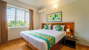 A hotel room with a large bed, a nightstand with a lamp, a framed abstract art piece, and a window with curtains. -  Treebo Classic Highway Side (Thiruvananthapuram)
