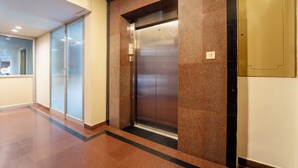 A modern elevator with a metallic finish, flanked by glass doors and a marble wall. -  Treebo Classic Highway Side (Thiruvananthapuram)