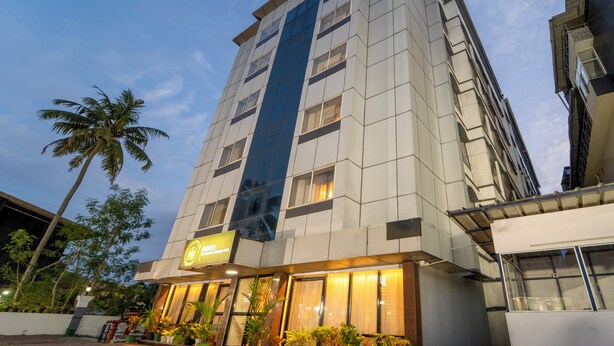 A modern hotel with a prominent vertical glass facade, multiple floors, and a well-lit entrance. -  Treebo Classic Highway Side (Thiruvananthapuram)