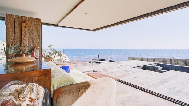 Un balcón amplio con vistas al mar, una mesa de madera con plantas y un rincón de estar acogedor.