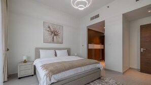 Une chambre à coucher moderne avec un grand lit, des tables de chevet, une œuvre d’art accrochée au mur et une armoire en bois.