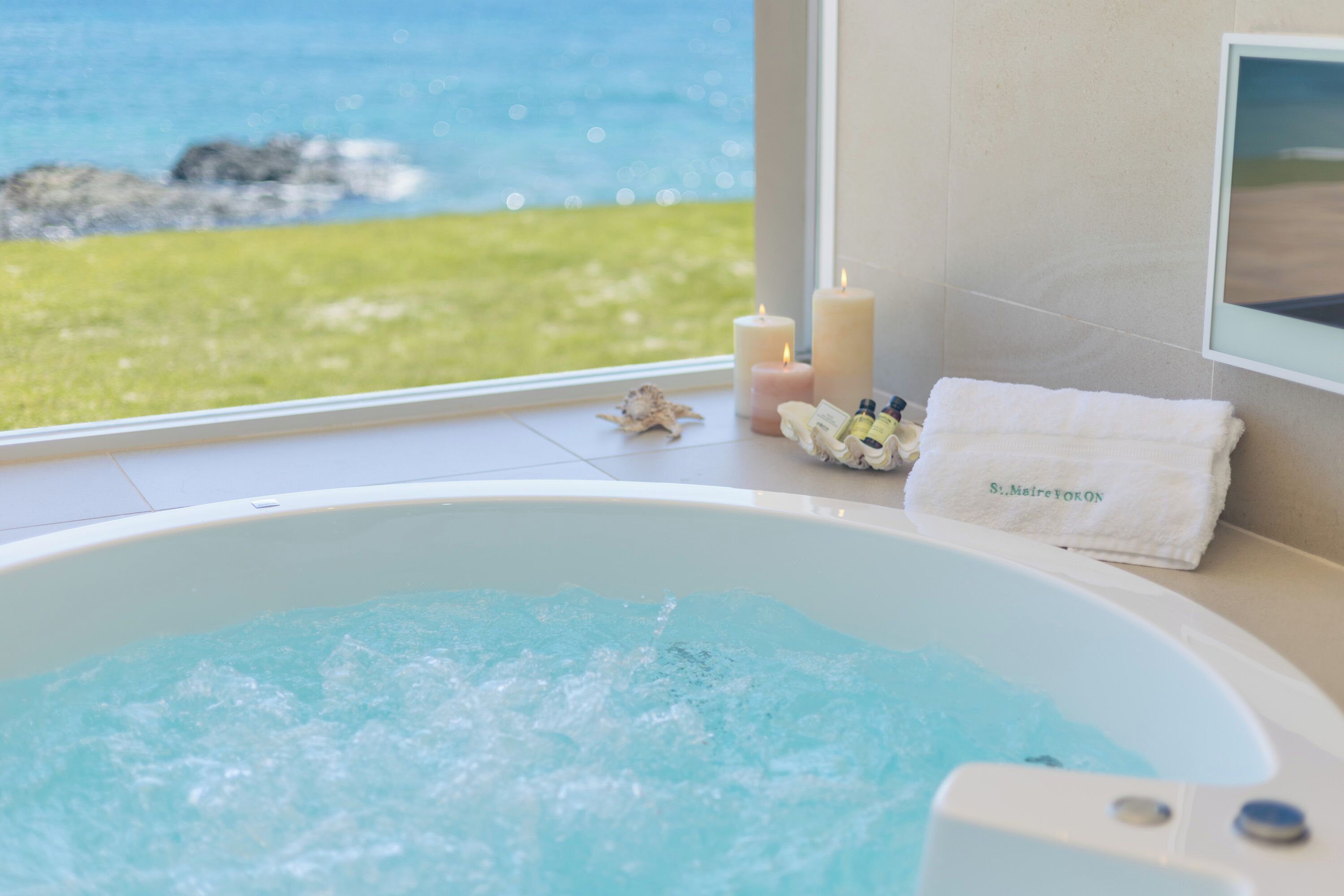 A bathtub with a view of the sea, a towel, and candles.
