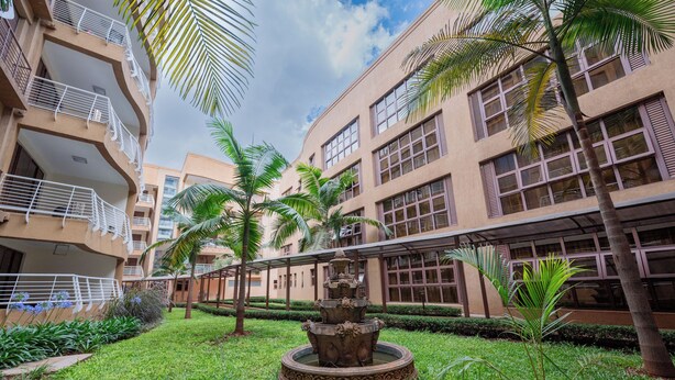 Un cortile con una fontana al centro, circondato da palme e un edificio con balconi.