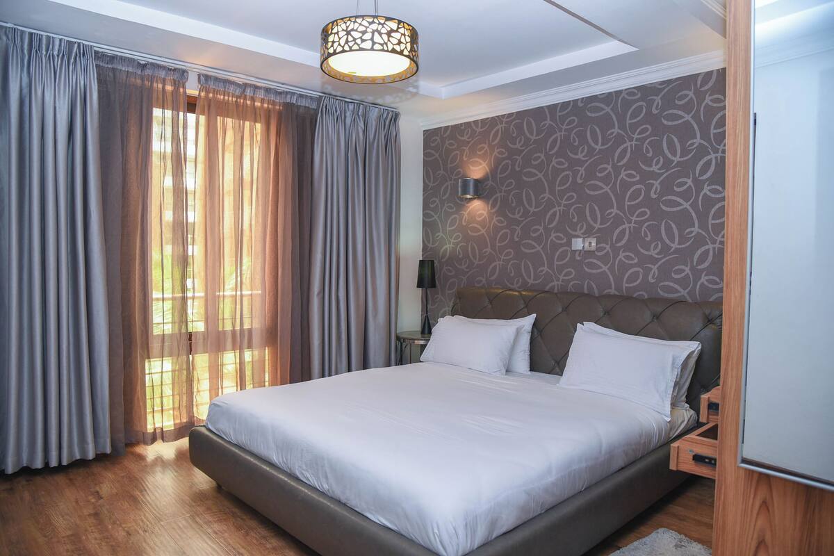 Moderni hotellihuone, jossa on suuri sänky, kuvioitu seinä ja ikkuna, jossa on verhot.