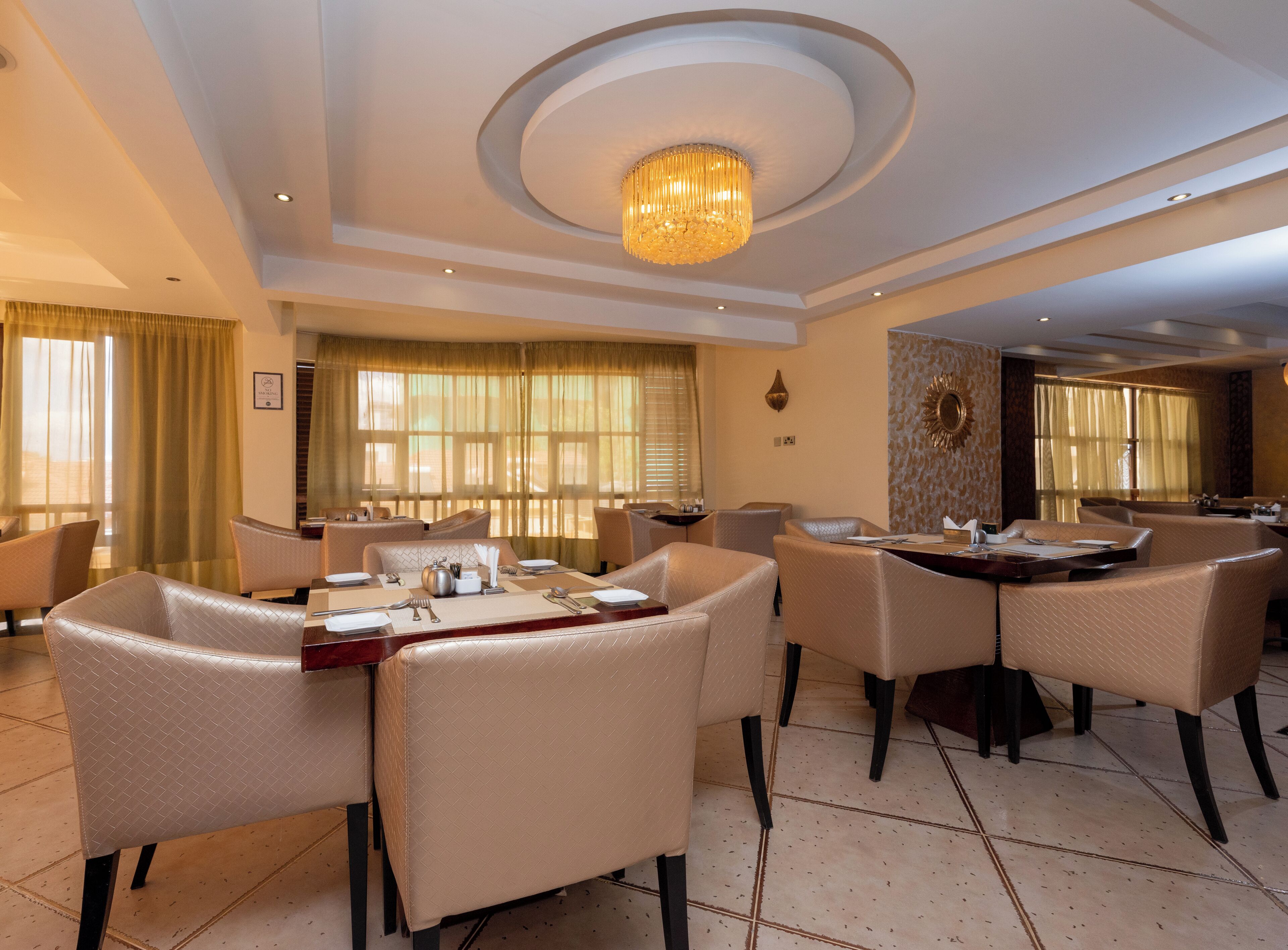 Un espace de restauration d’hôtel avec des tables rondes, des chaises rembourrées et un lustre.