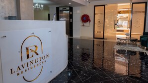 Un'area di accoglienza con pavimento in marmo lucido, un lampadario e una reception con il logo 'LAVINGTON RESIDENCES'.