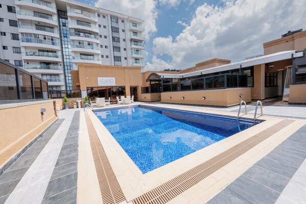 Uma piscina com um deck revestido, rodeada por um edifício moderno com varandas e uma placa com a inscrição 'SCAFF'.