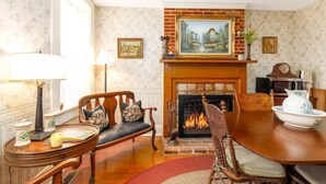A traditional living room with a fireplace, a dining table, and a sofa. - Briarstone Inn | Historic 7-Room Inn w/ Private Baths | Walk to Downtown Galena (Galena)