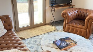 Un salon avec un canapé en cuir marron, une table basse ronde et un téléviseur posé sur un meuble.