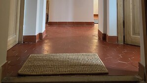 Un couloir avec une affiche encadrée accrochée au mur, une main courante en bois et un paillasson à l’entrée.