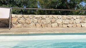 Une piscine à l’eau claire, un mur de pierre et des arbres en arrière-plan.