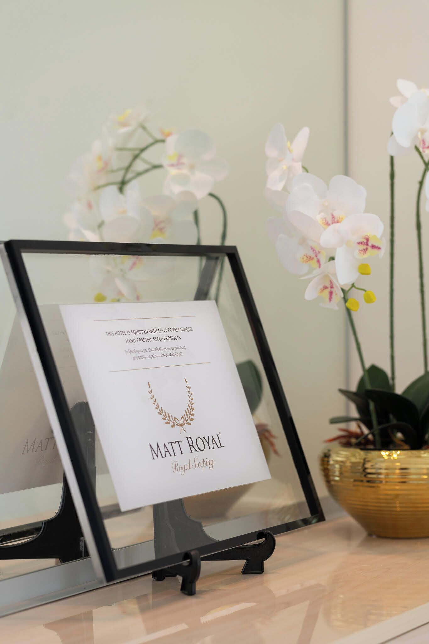 Um letreiro emoldurado com texto sobre produtos Matt Royal Royal Sleepyhead, um suporte preto e orquídeas brancas ao fundo.