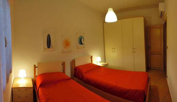 A bedroom with two beds, a wardrobe, and a nightstand with a lamp.