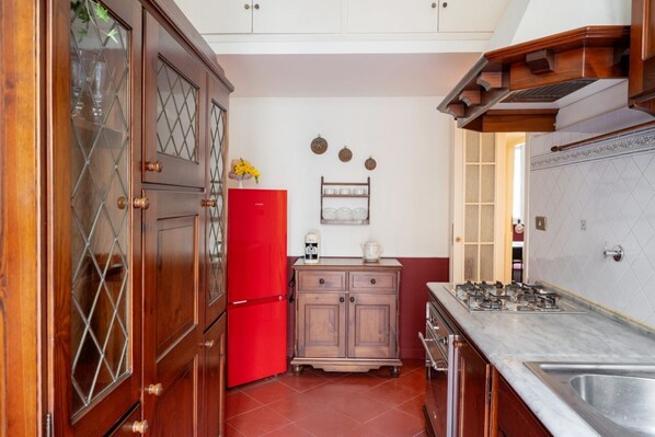 A compact kitchen with wooden cabinets, a red refrigerator, a gas stove, and a small countertop. - Maroon Flat Colosseo, 800 mt from Amphitheater (Roma)