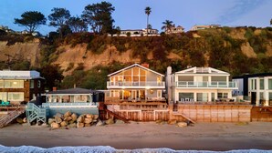 Une propriété située en bord de mer, dotée d’une terrasse en bois, d’une grande maison avec balcon et d’un bâtiment plus petit.