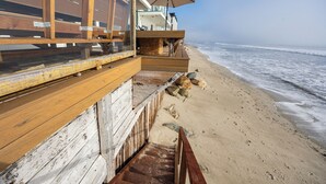 Un escalier en bois menant à un balcon donnant sur la plage, agrémenté d’un parasol.