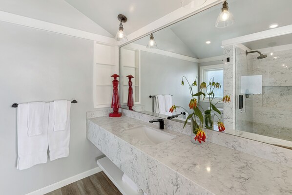 A modern bathroom with a marble sink, a large mirror, and a shower area.