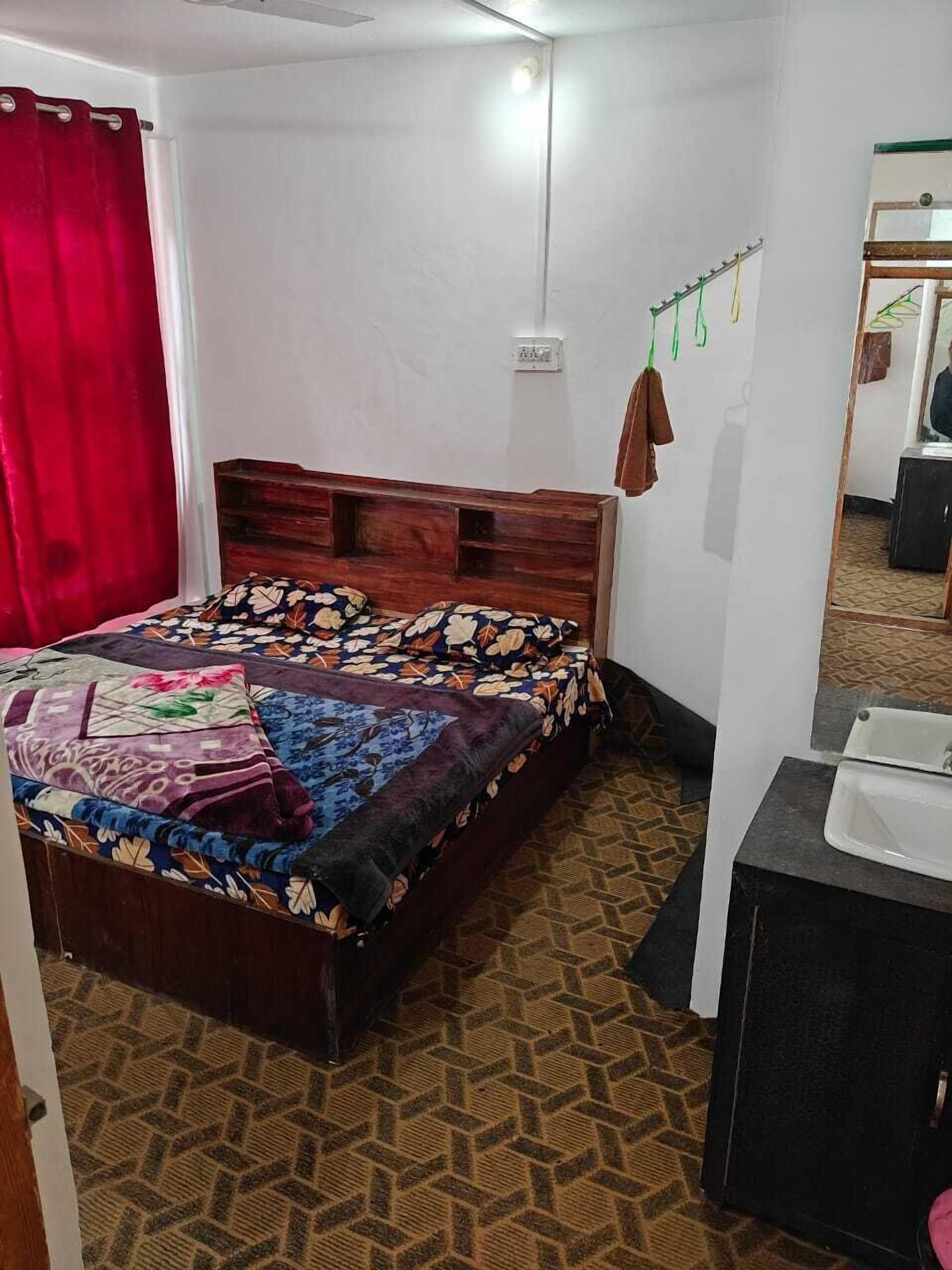 Un dormitorio con una cama de madera, una cortina roja, un espejo y un baño pequeño con un lavamanos.