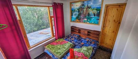 A room with a bed, a ceiling fan, a painting, and a window with curtains.