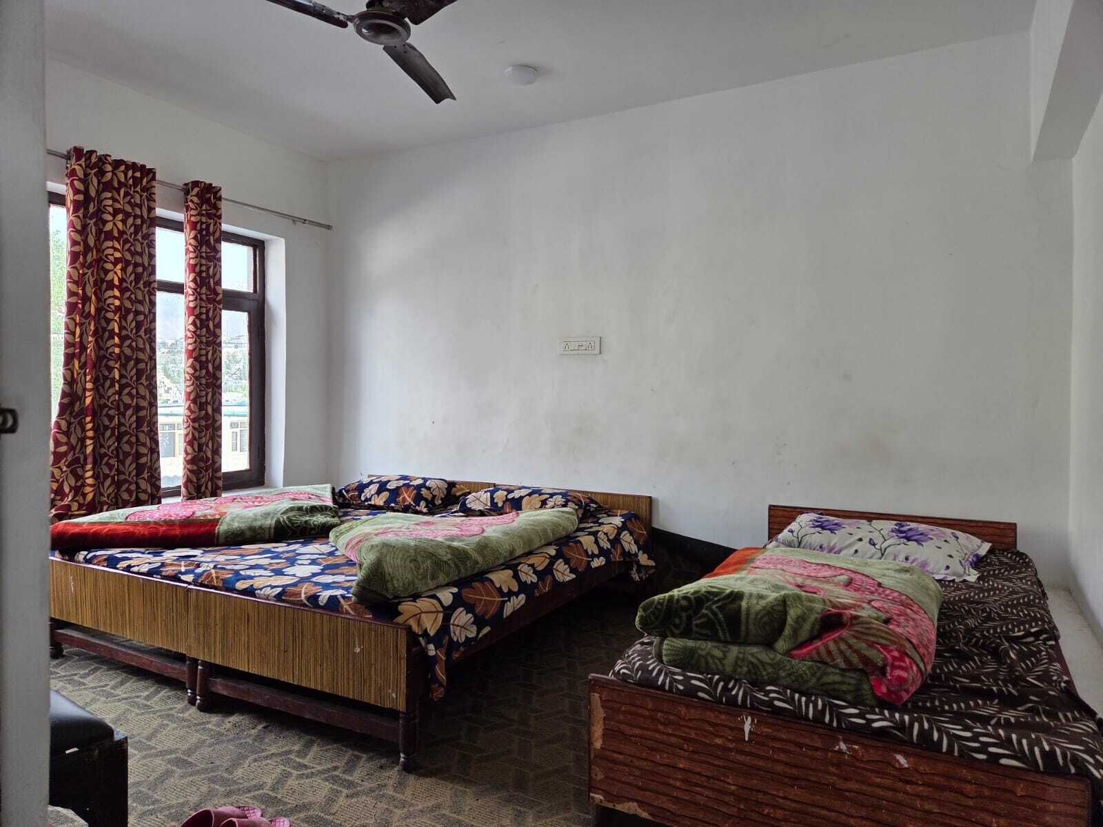 A room with two beds, a ceiling fan, and a window with curtains.