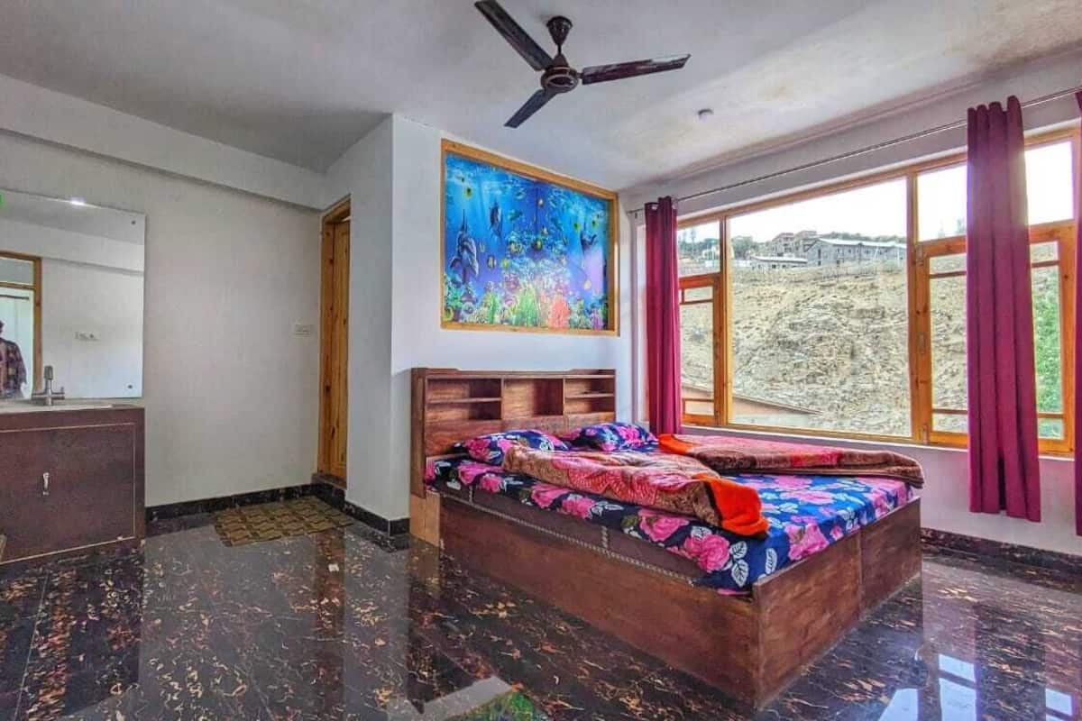 Un dormitorio con cama, ventilador de techo, un cuadro, ventana con cortinas y vista al exterior.