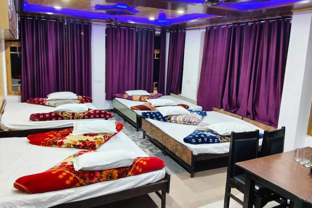 Habitación de hotel con dos camas, cortinas moradas, ventilador de techo y una mesa de comedor con sillas.