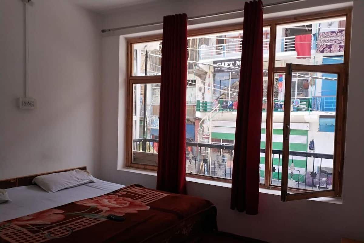 Una habitación con cama, ventana con cortinas y vista a un edificio.