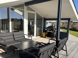 An outdoor patio with a table and chairs, a grill, and a sliding glass door leading to a covered area.