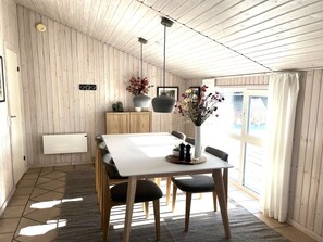 Een eetgedeelte met een witte tafel, vier stoelen, een vaas met bloemen en een houten kast.
