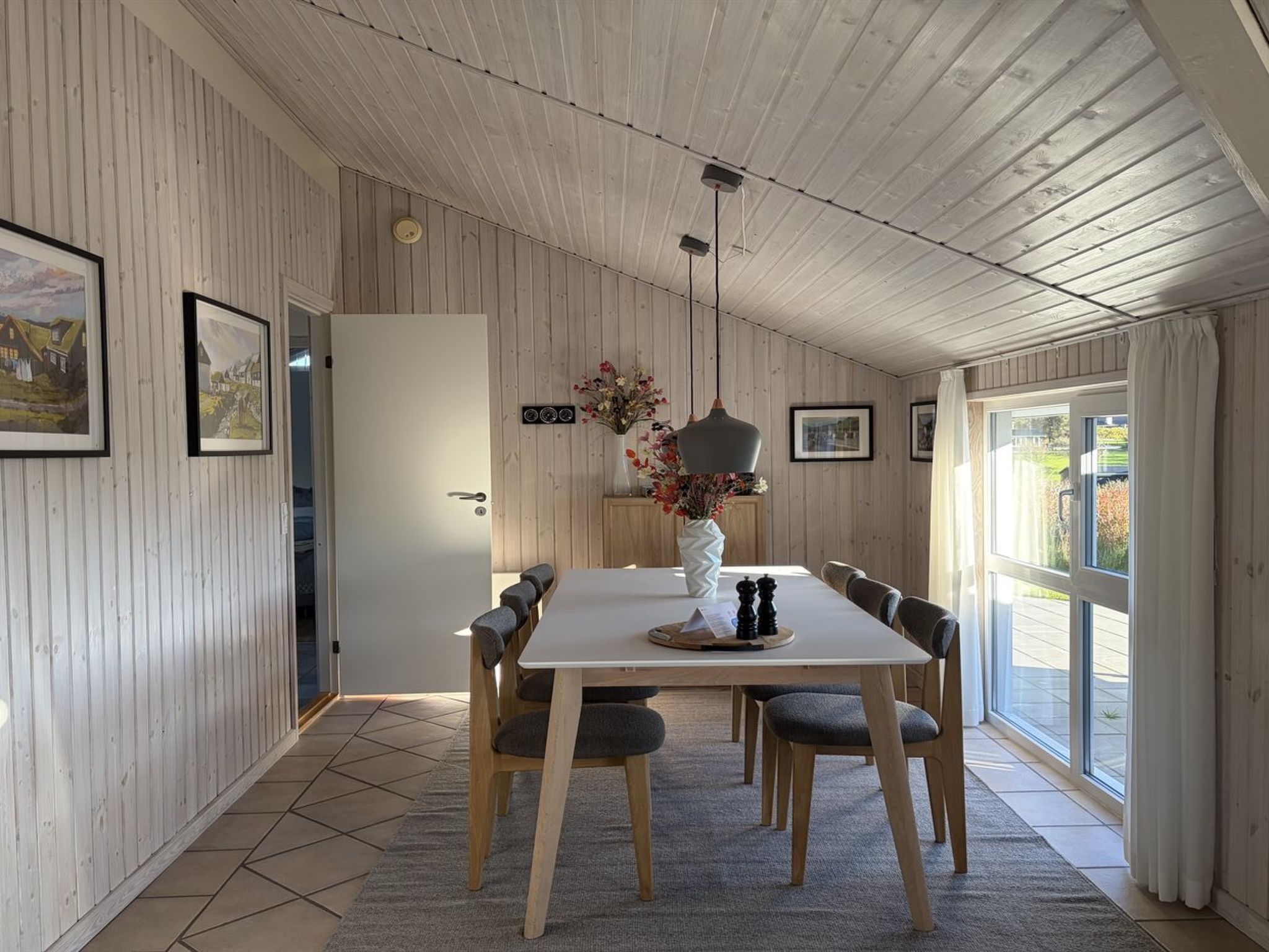 Un coin repas avec une table en bois, des chaises, un vase de fleurs et une suspension.