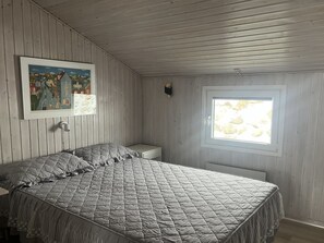 Een slaapkamer met een bed, een nachtkastje, een raam met uitzicht en twee ingelijste foto's aan de muur.