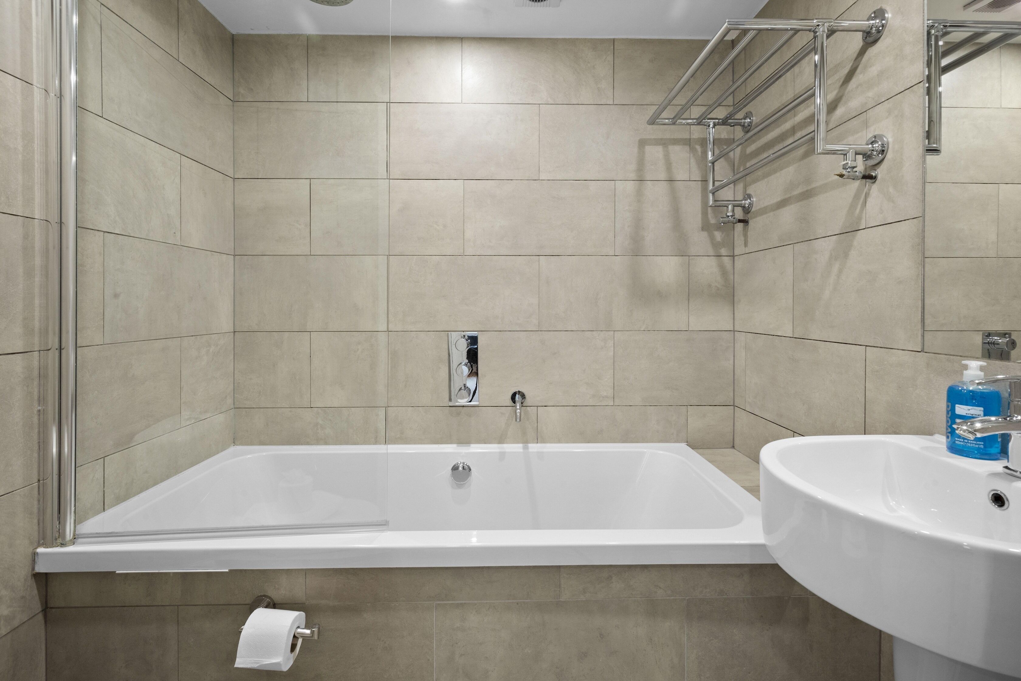 Uma casa de banho moderna com banheira, lavatório e suporte para papel higiénico.