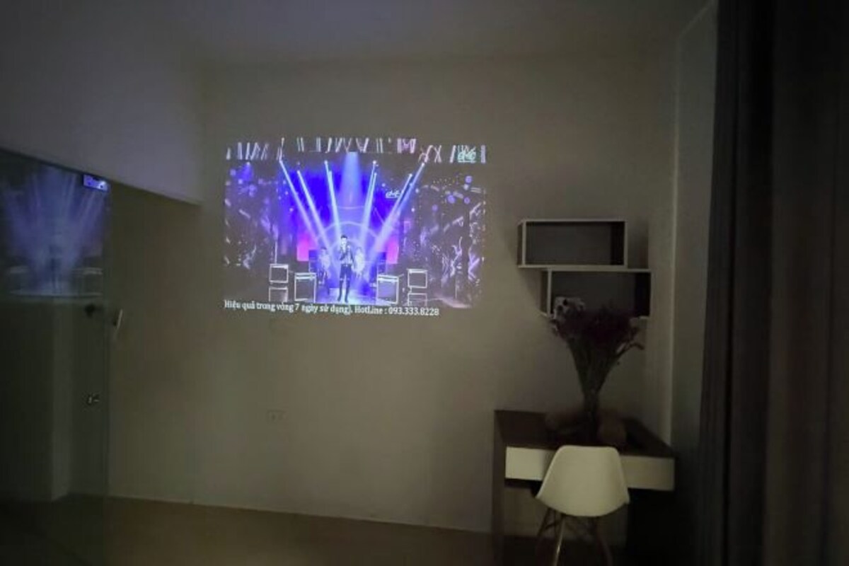 Ein Raum mit einem an der Wand befestigten Projektor, der eine Präsentation zeigt, einem weißen Stuhl und einem kleinen Tisch mit einer Vase.