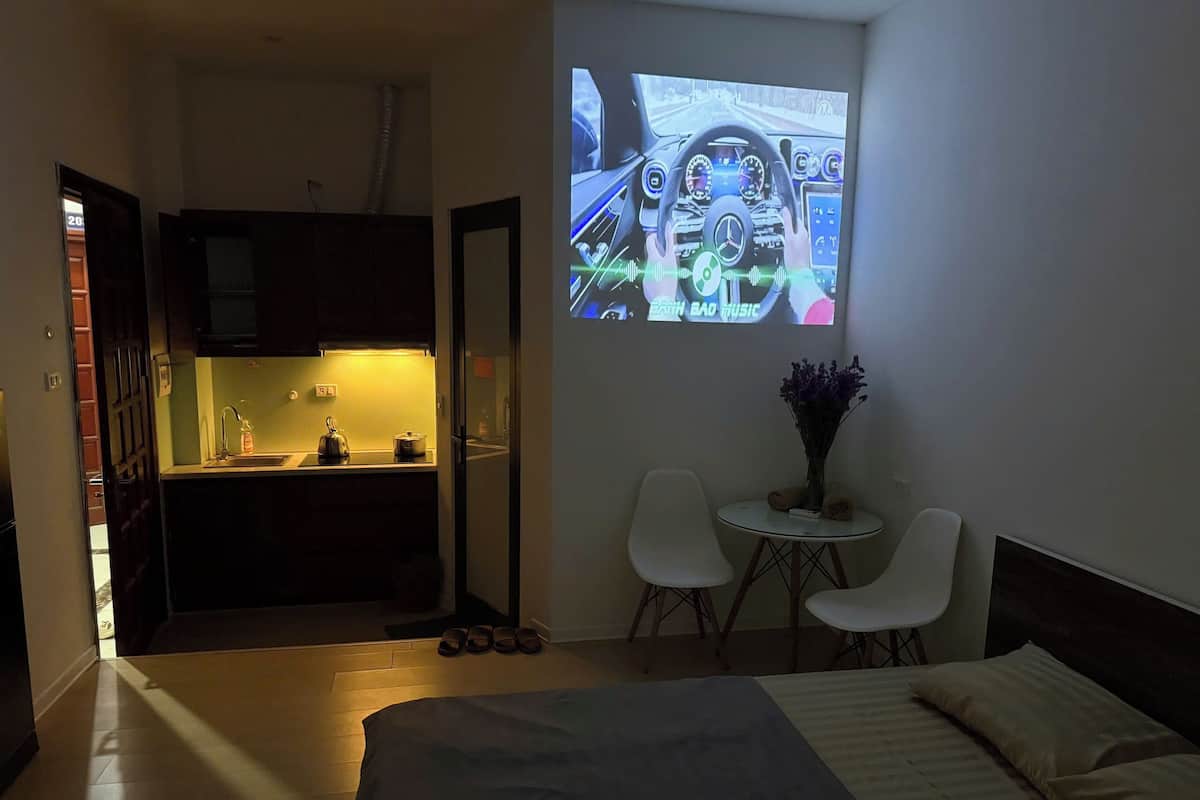 A hotel room with a bed, a small table with chairs, a kitchen area, and a wall projection.