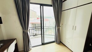A room with a sliding glass door leading to a balcony, a white wardrobe, and a desk with a telephone. - Era Apartment Chua Ha (Hanoi)