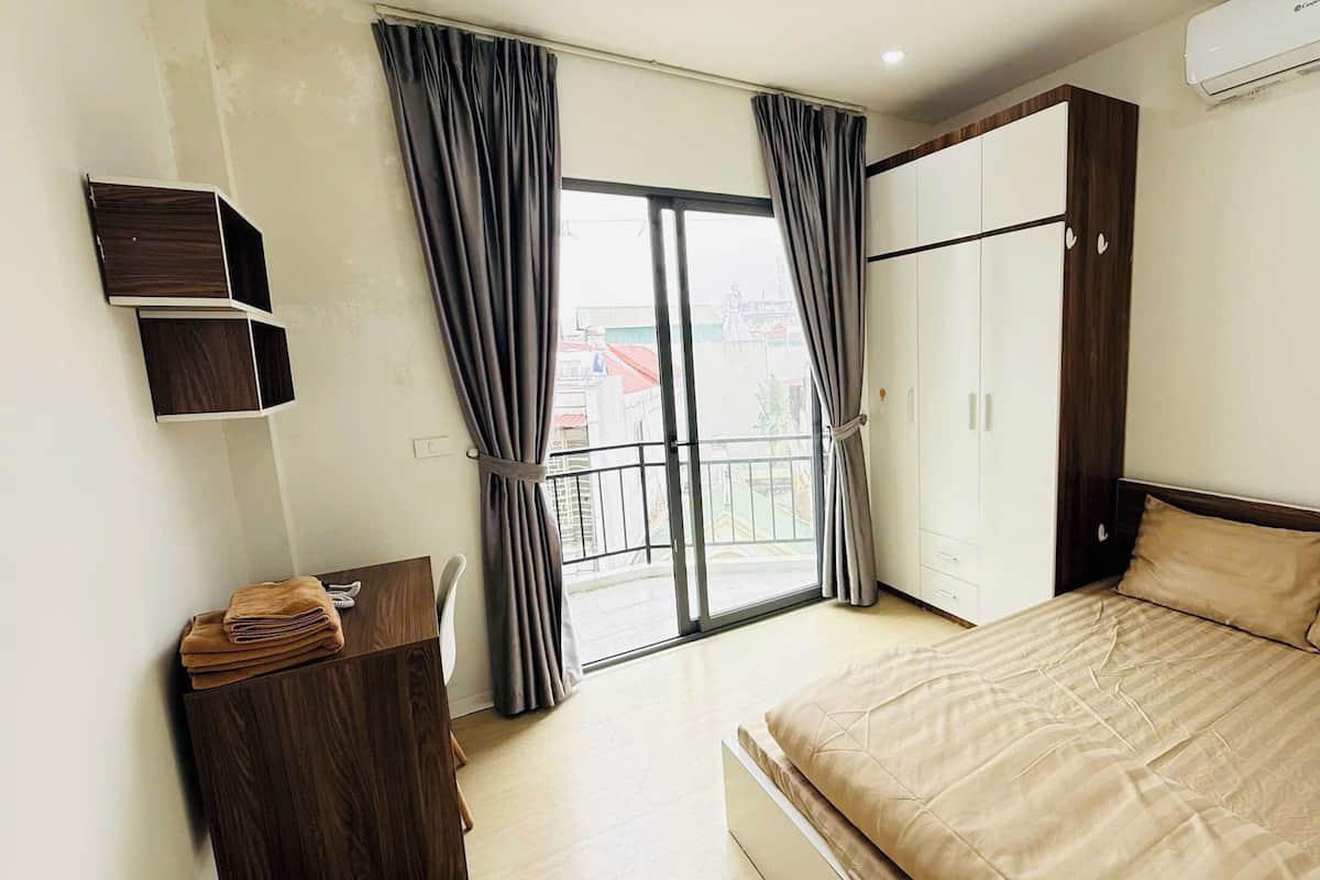 A bedroom with a bed, a wardrobe, a desk, and a balcony with curtains.