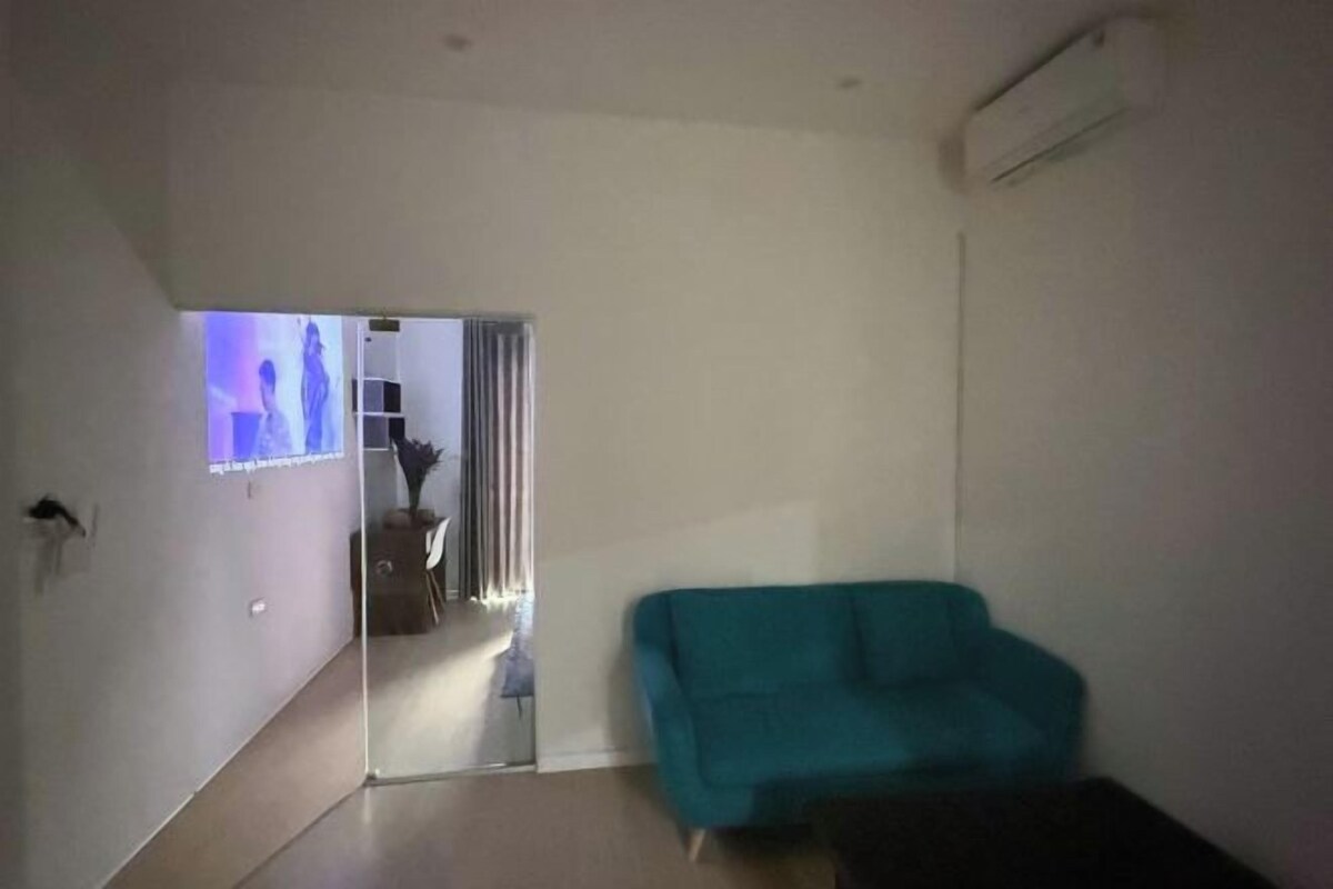 A living room with a teal sofa, a glass partition, and a television displaying a show.