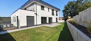 Una casa moderna de dos pisos con techo plano, grandes puertas correderas y un pequeño patio con mobiliario exterior.