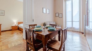 Ein Essbereich mit Holztisch, gedeckt für vier Personen, einer Couch und einem Bett im Hintergrund.