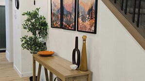 Een hal met een houten console tafel, een potplant en drie ingelijste foto’s aan de muur.