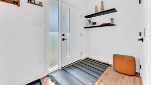 Een modern interieur met een witte deur, zwarte planken met decoratieve objecten, een blauw patroon tapijt en een houten bankje.