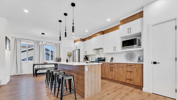 Een moderne keuken met witte kasten, houten accenten, een centraal eiland en barstoelen.