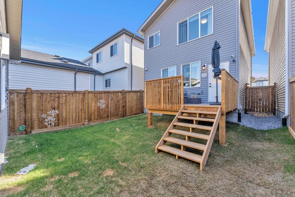 A residential backyard with a wooden deck, a set of stairs leading to a house entrance, and a fenced area. - Cozy Rustic House(pet friendly/garage/backyard) (Beaumont)