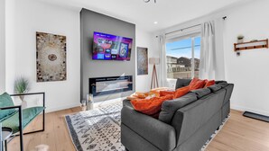 Een moderne woonkamer met een grijze bank, een flatscreen televisie en een groot raam.