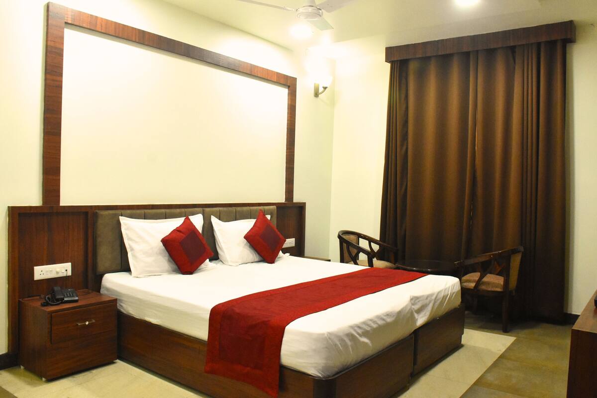 A hotel room with a large bed, a nightstand with a phone, a desk, and a chair.