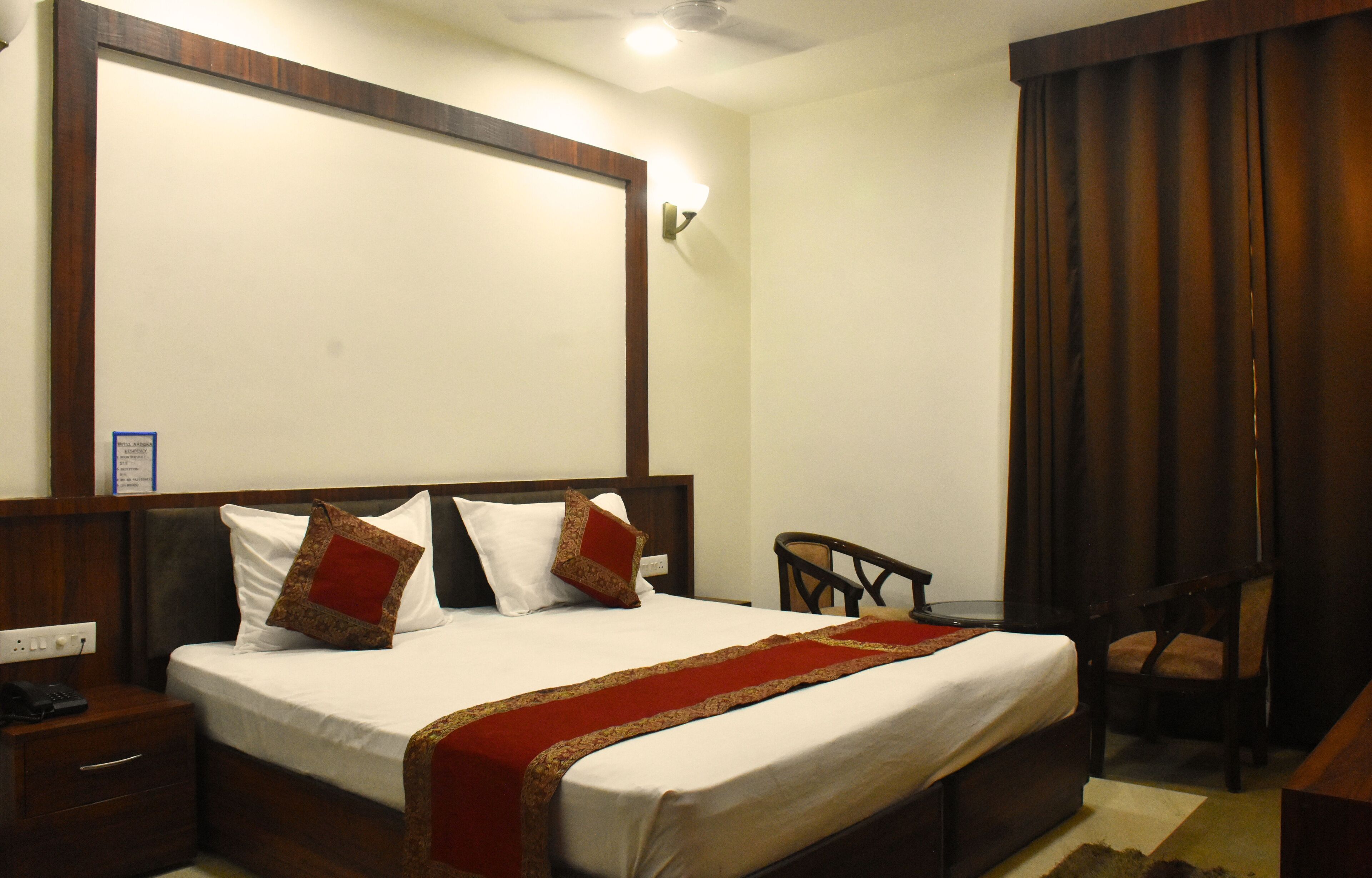 A hotel room with a large bed, a wooden headboard, a bedside table with a phone, and a chair.