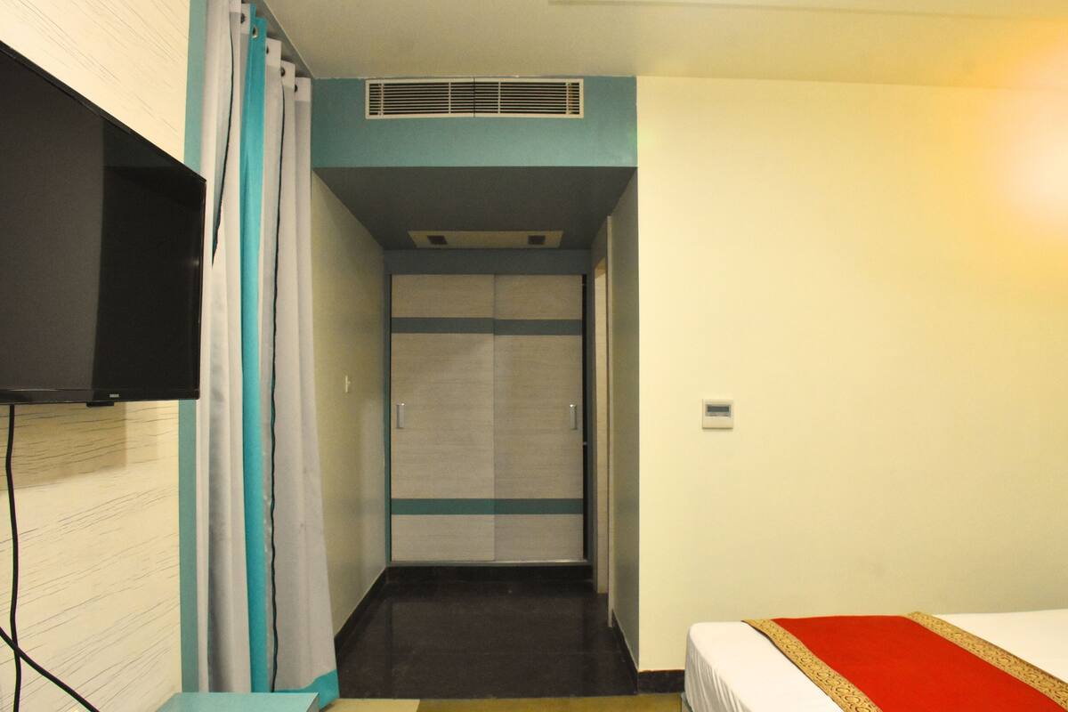 A narrow hallway with a bed on the right, a television on the left, and a door at the end.